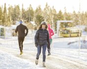 Tre personer går/joggar på en trottoar en snöig solig dag.